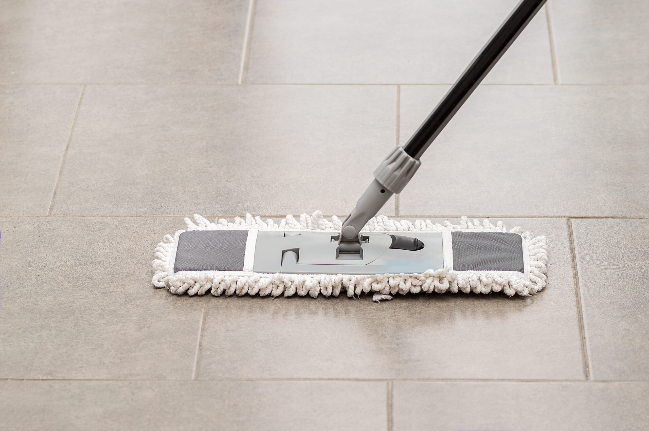 Microfiber mop cleaning a porcelain tiled floor with light grout lines
