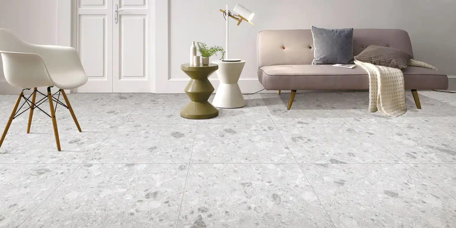 Modern living room with large light gray terrazzo floor tiles with thin matching grout, a beige tufted sofa, and two sculptural side tables with decor.