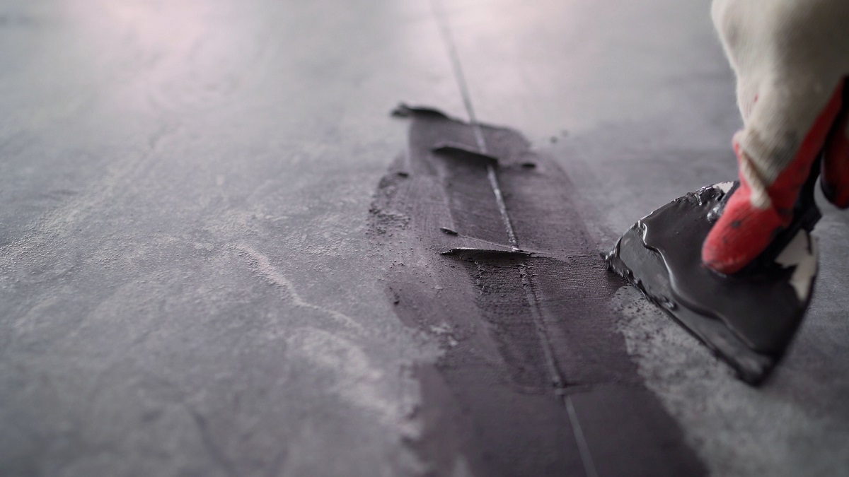 Close-up of dark grout being applied to a gray textured tile floor with a grout float.